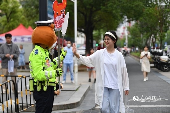 6月7日上午9時(shí)，隨著鈴聲的響起，2023年江西高考正式開考，江西省的53.57萬考生以縣（區(qū)）為單位隨機(jī)安排在全省256個(gè)考點(diǎn)、18968個(gè)考場(chǎng)參加高考。圖為“小熊交警”和考生擊掌鼓勵(lì)。 人民網(wǎng)記者 時(shí)雨攝