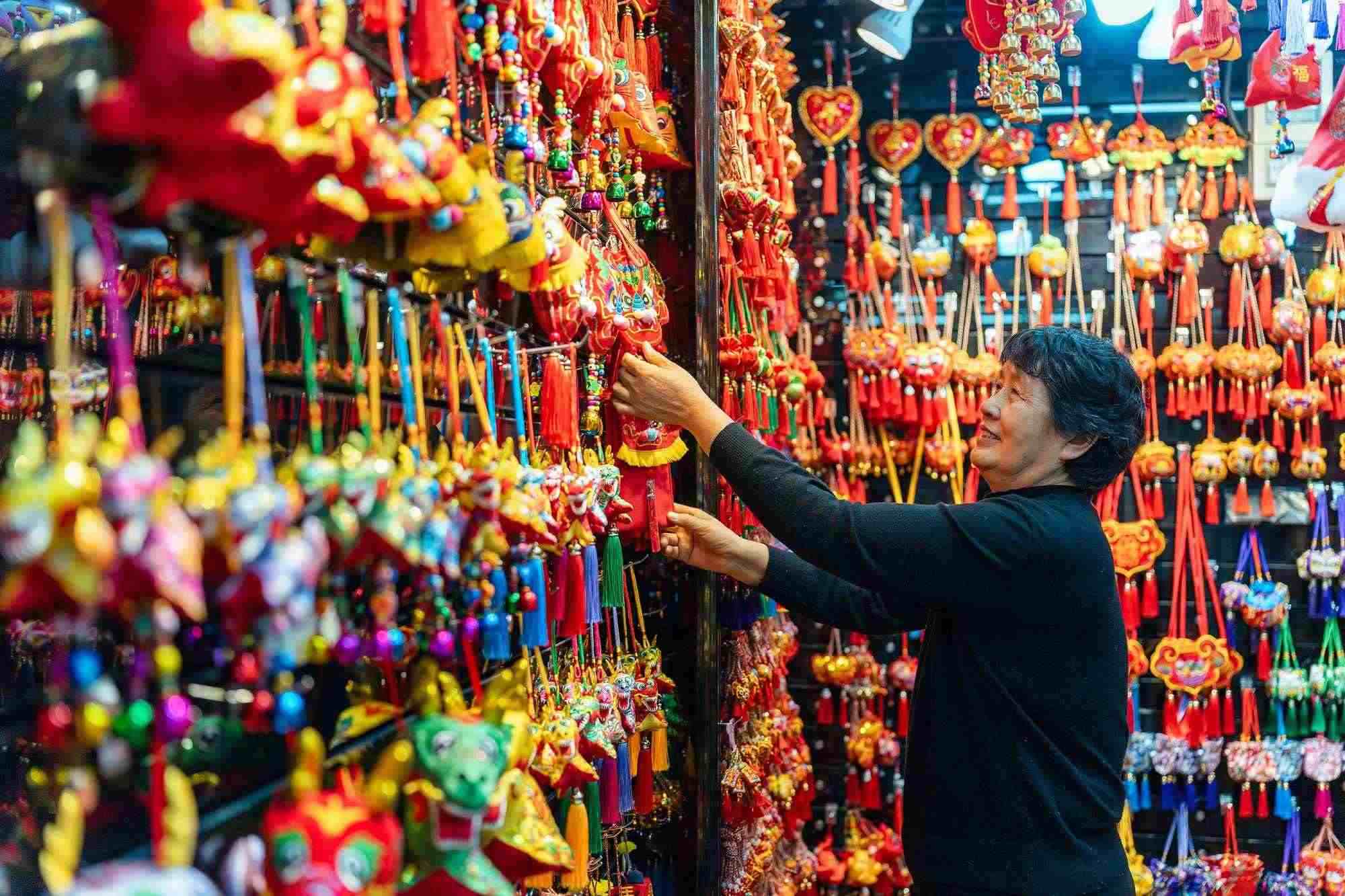 2023年12月11日，金華義烏國際商貿(mào)城，龍年喜慶用品掛滿攤位，顧客正在挑選中。