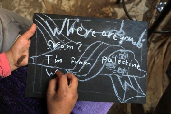 2023年12月28日，一名學(xué)生在加沙地帶南部城市拉法一所學(xué)校的臨時教室中寫下“我來自巴勒斯坦”的字樣。新華社發(fā)（里澤克·阿卜杜勒賈瓦德攝）