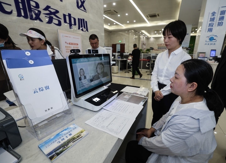 在浙江省嘉興市秀洲區(qū)王江涇鎮(zhèn)便民服務中心的“跨域通辦·云綜窗”窗口，辦理開業(yè)登記的個體工商戶（右一）通過該系統(tǒng)與江蘇省蘇州市吳江區(qū)盛澤鎮(zhèn)行政審批局工作人員視頻連線，進行身份讀取及材料線上審核（2024年5月9日攝）。新華社記者 徐昱 攝